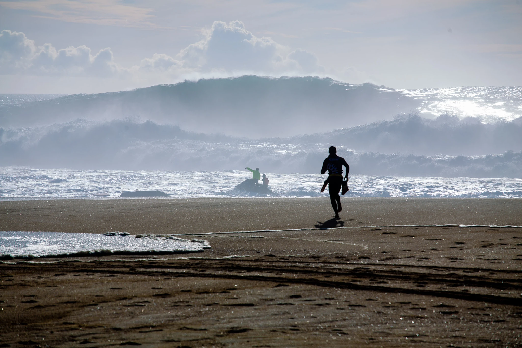 A figure sprints across the wet sand toward a jet ski in the surf, a towering wave looming behind them, the whole beach lit in a cold glittering haze.